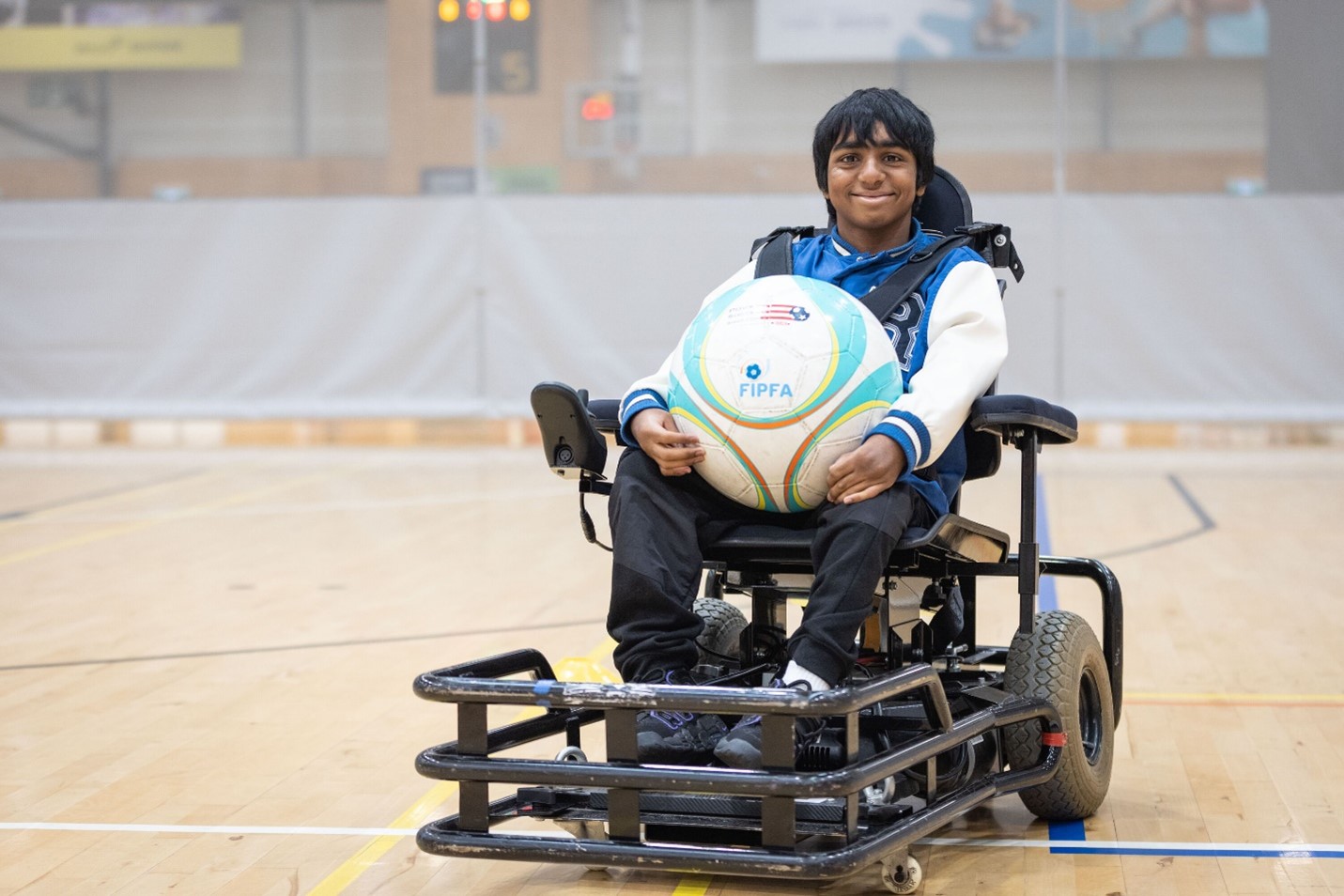 Ashmit on a powerchair football court holding the ball in his lap